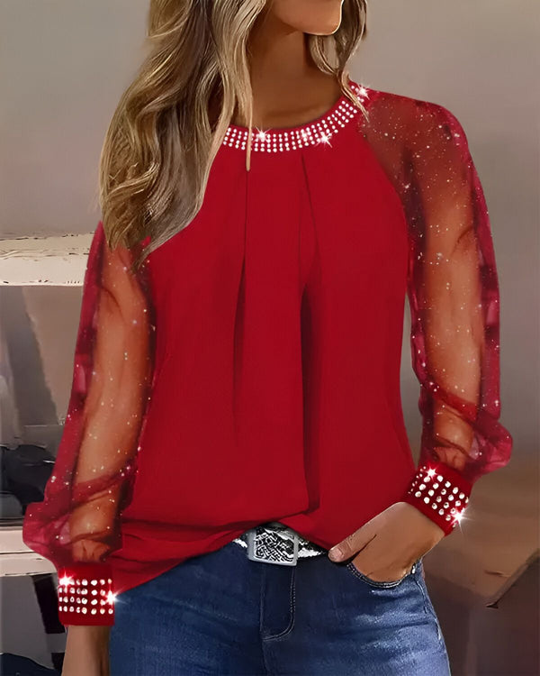 Une femme porte un chemisier rouge à manches longues et transparentes. Le chemisier est orné de strass au niveau du col et des poignets.