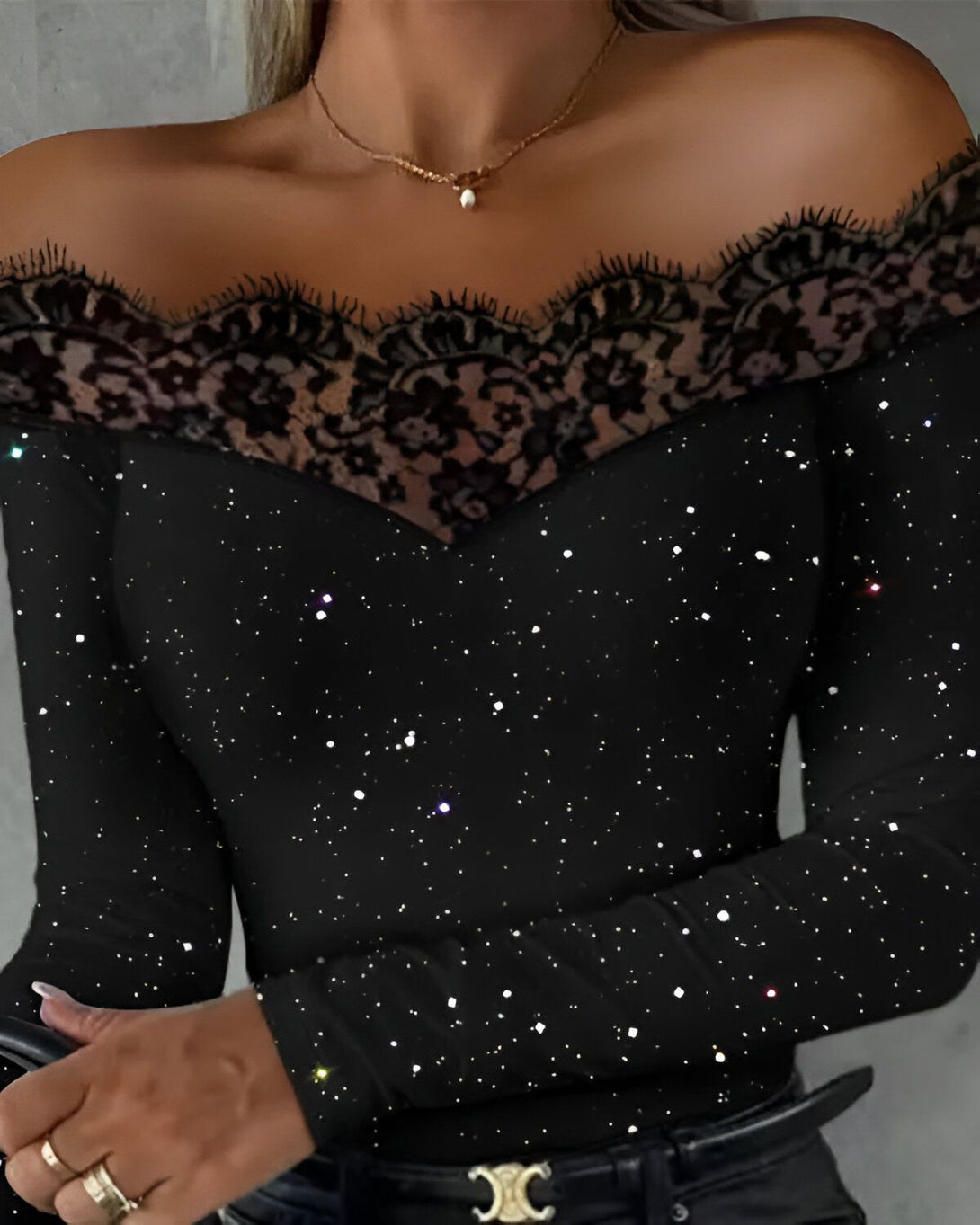 Une femme porte un haut noir à épaules dénudées avec des détails en dentelle noire. Le haut est scintillant et a un col en V.