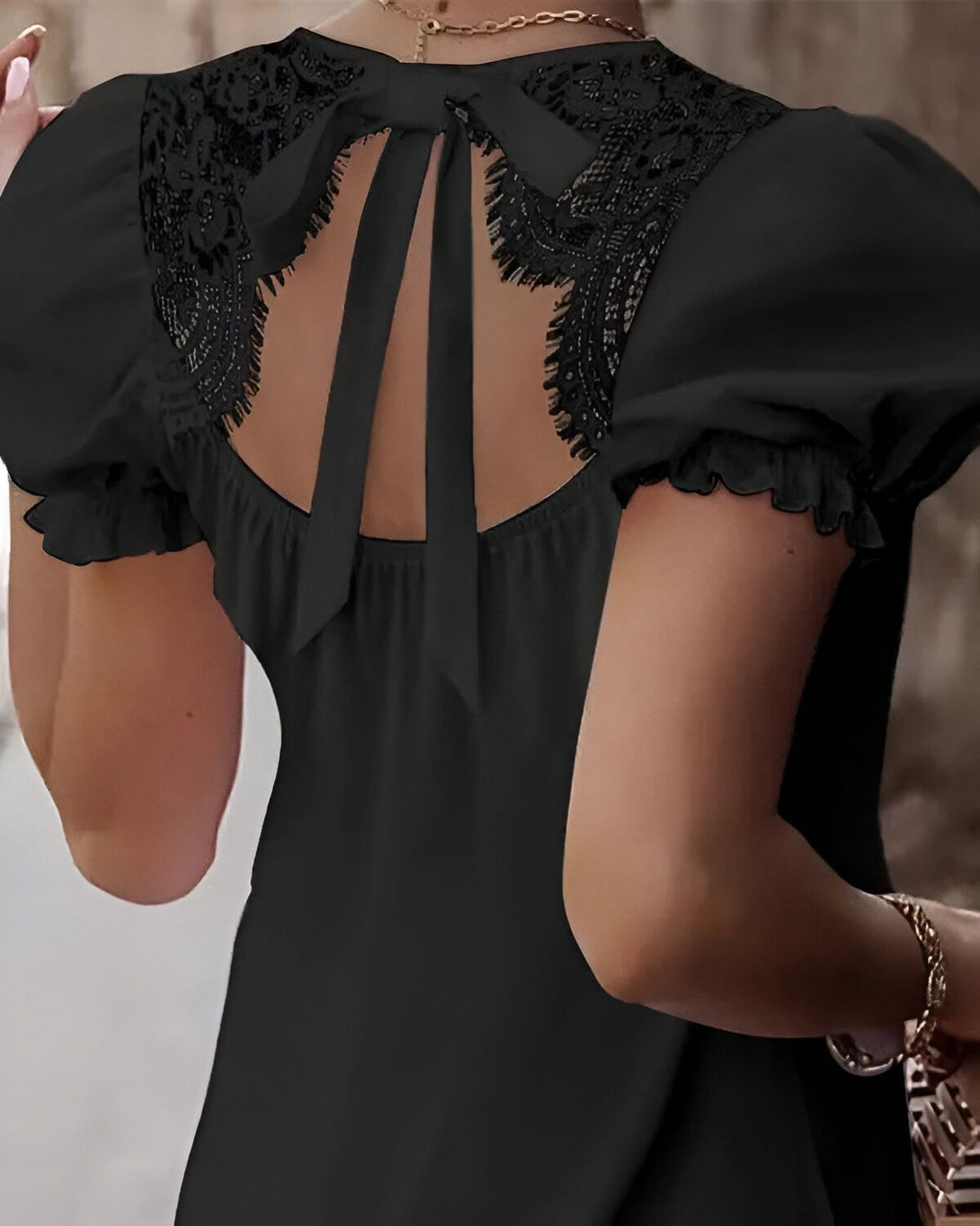 Une femme porte un chemisier noir avec des manches bouffantes et un dos en dentelle.