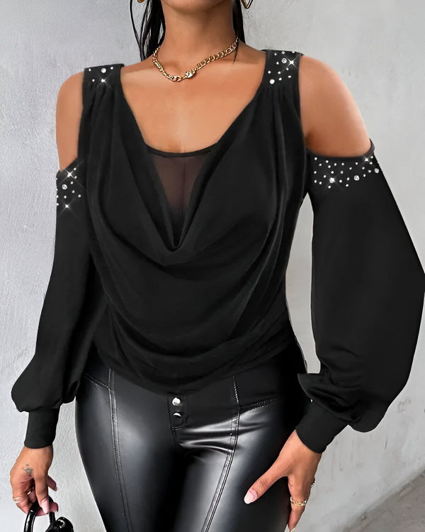 Une femme porte un chemisier noir à col montant et à épaules dénudées. Le chemisier est en mousseline de soie et est transparent au niveau des épaules. La femme porte également un pantalon en cuir noir et un collier doré.