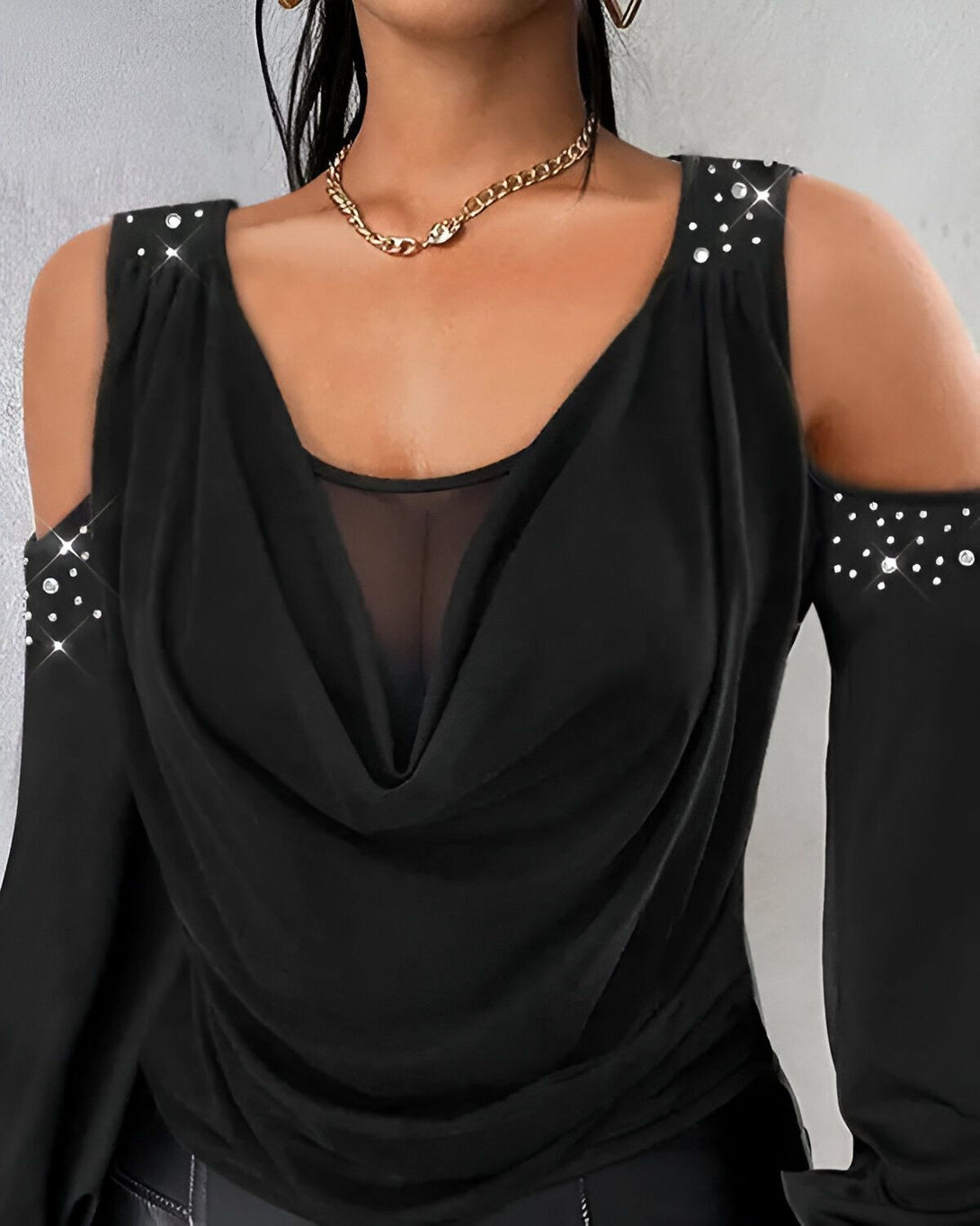 Une femme porte un chemisier noir à épaules dénudées. Le chemisier est en mousseline de soie et a un décolleté en V. Il est orné de strass sur les épaules.