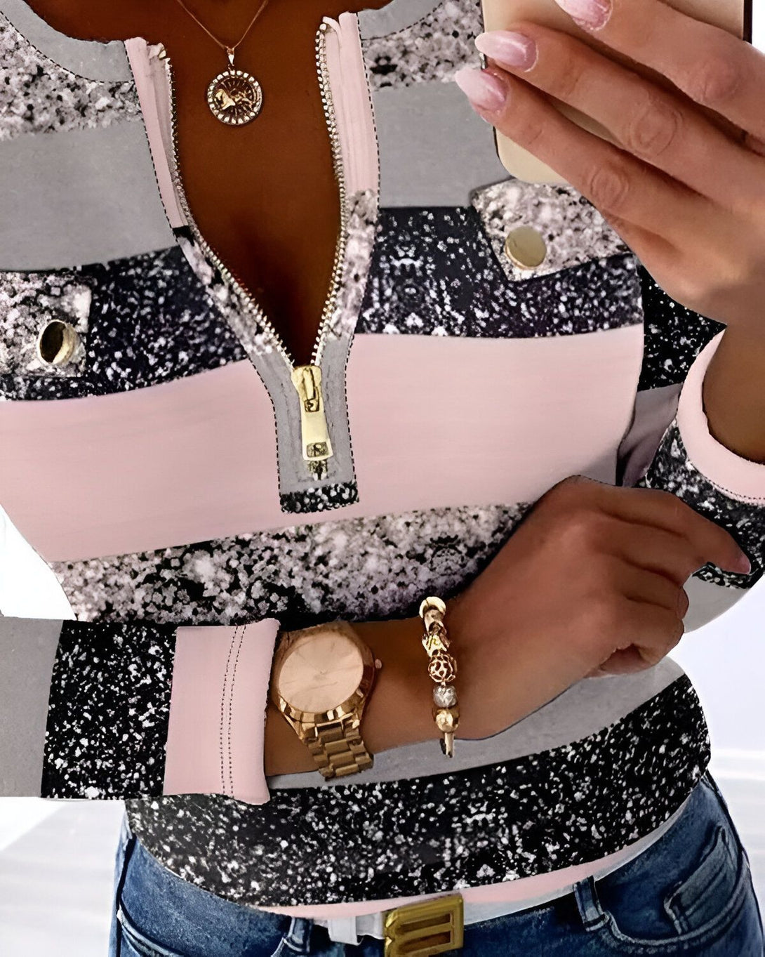 Une femme porte un haut moulant à manches longues avec un col montant et une fermeture éclair sur le devant. Le haut est gris, rose et noir avec un motif de paillettes.