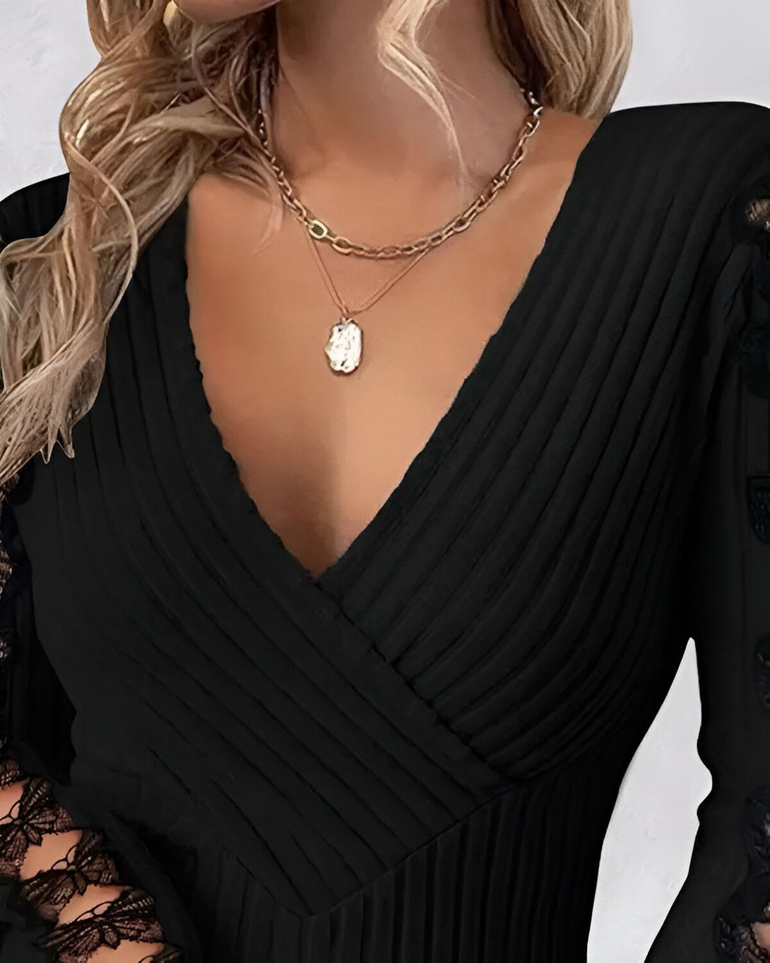 Une femme porte une robe noire décolletée avec des manches en dentelle. Elle porte également deux colliers.