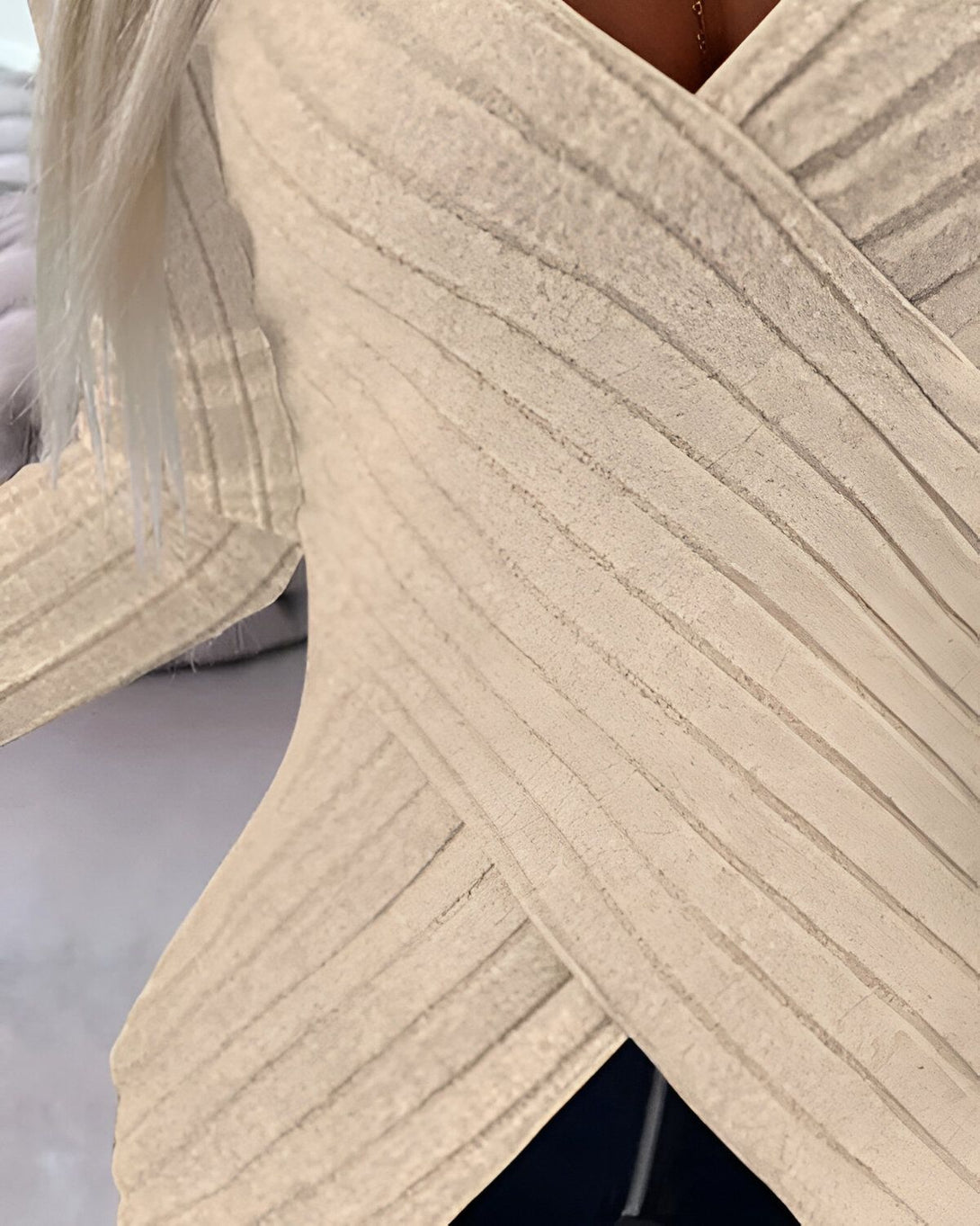 Une femme porte un haut beige croisé sur le devant. Le haut est côtelé et a des manches longues.