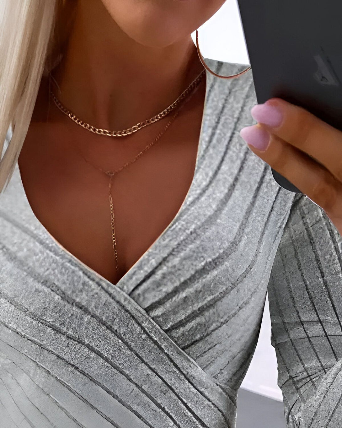 Une femme porte un chemisier gris décolleté croisé. Elle porte également deux colliers.