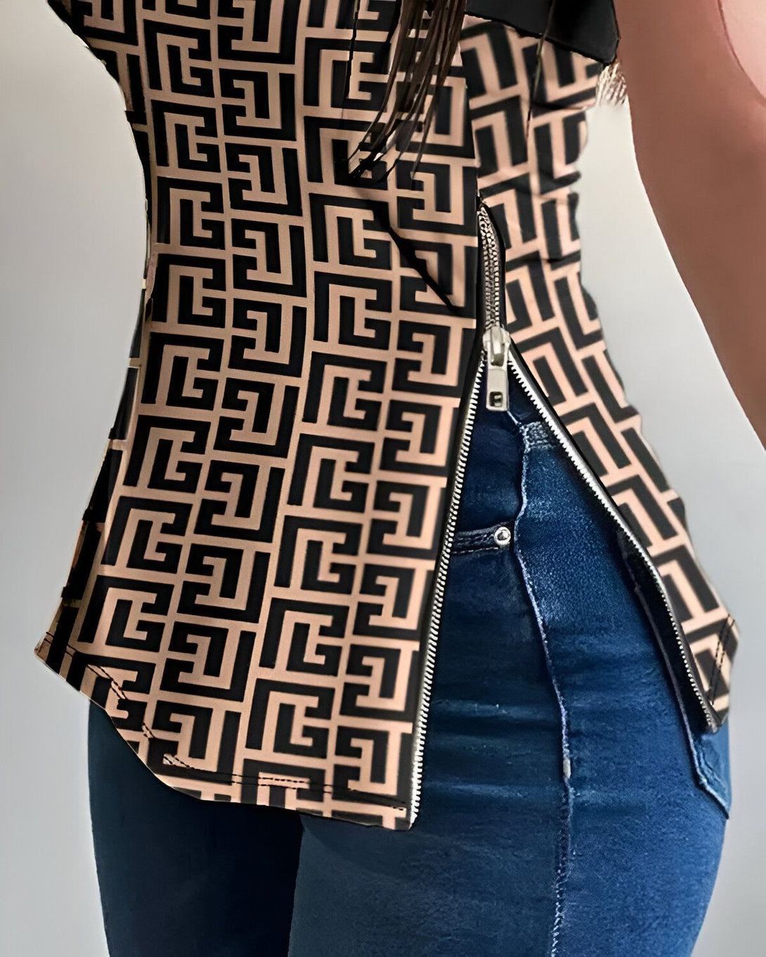 Une femme porte un chemisier marron et noir à motifs géométriques et une fermeture éclair sur le côté. Elle porte également un jean bleu.