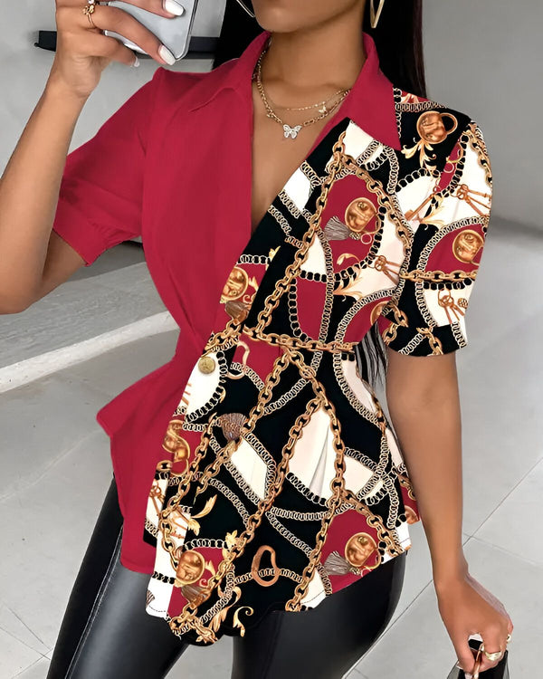 Une femme porte un chemisier rouge et noir. Le chemisier est décolleté en V et a des manches courtes. Il est noué sur le côté et a un imprimé chaîne. La femme porte également un pantalon noir et des talons noirs.