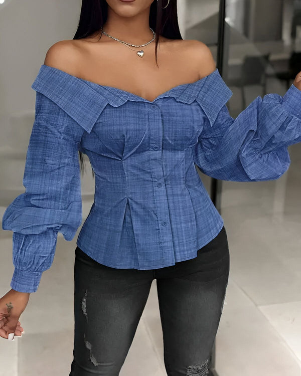 Une femme porte un chemisier bleu à épaules dénudées et des manches bouffantes. Le chemisier est boutonné sur le devant et froncé à la taille. Elle porte un jean noir déchiré et des talons noirs.
