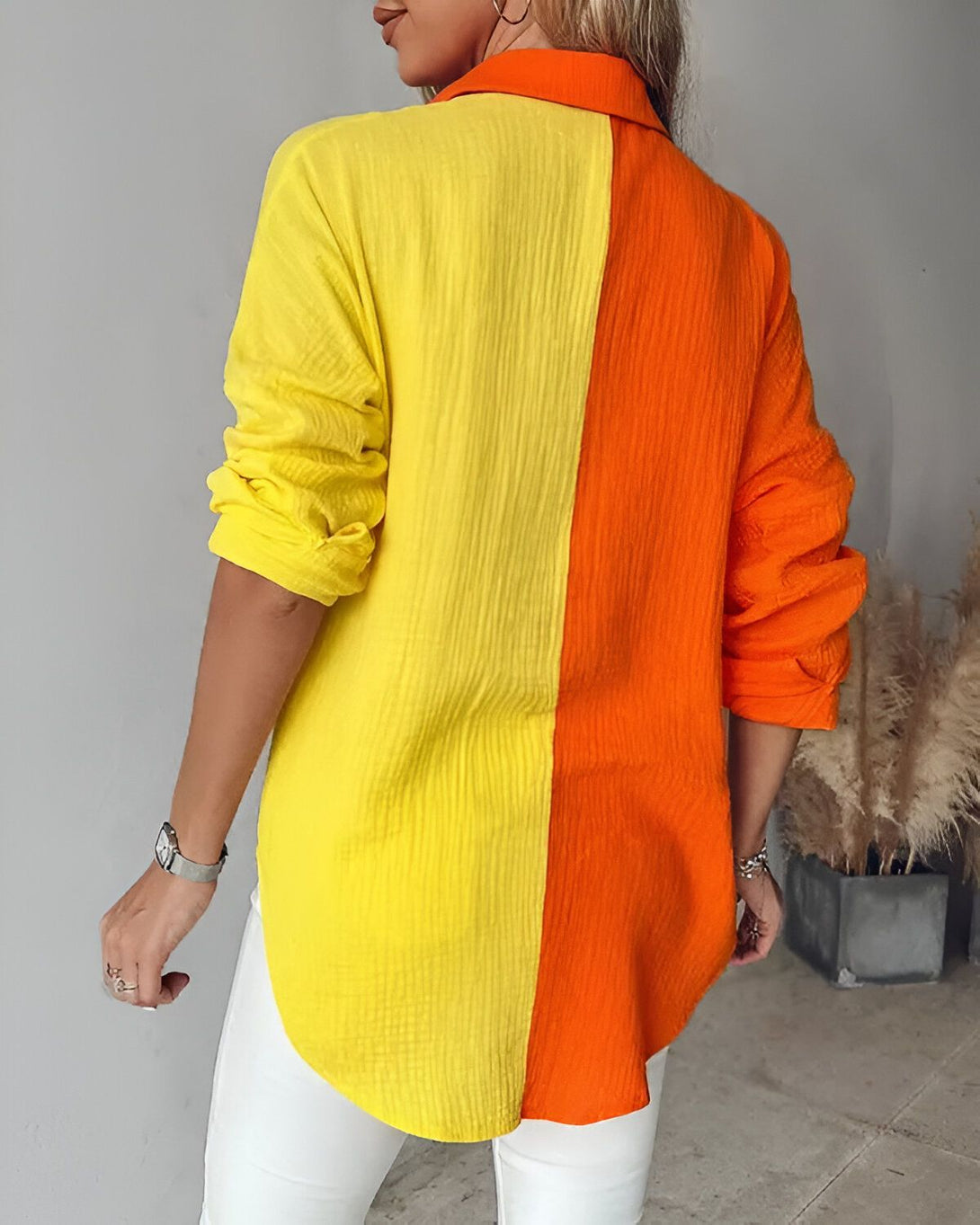 Une femme porte une chemise orange et jaune. La chemise est ouverte et on peut voir un t-shirt blanc en dessous. Elle porte également un jean blanc et des talons hauts blancs.