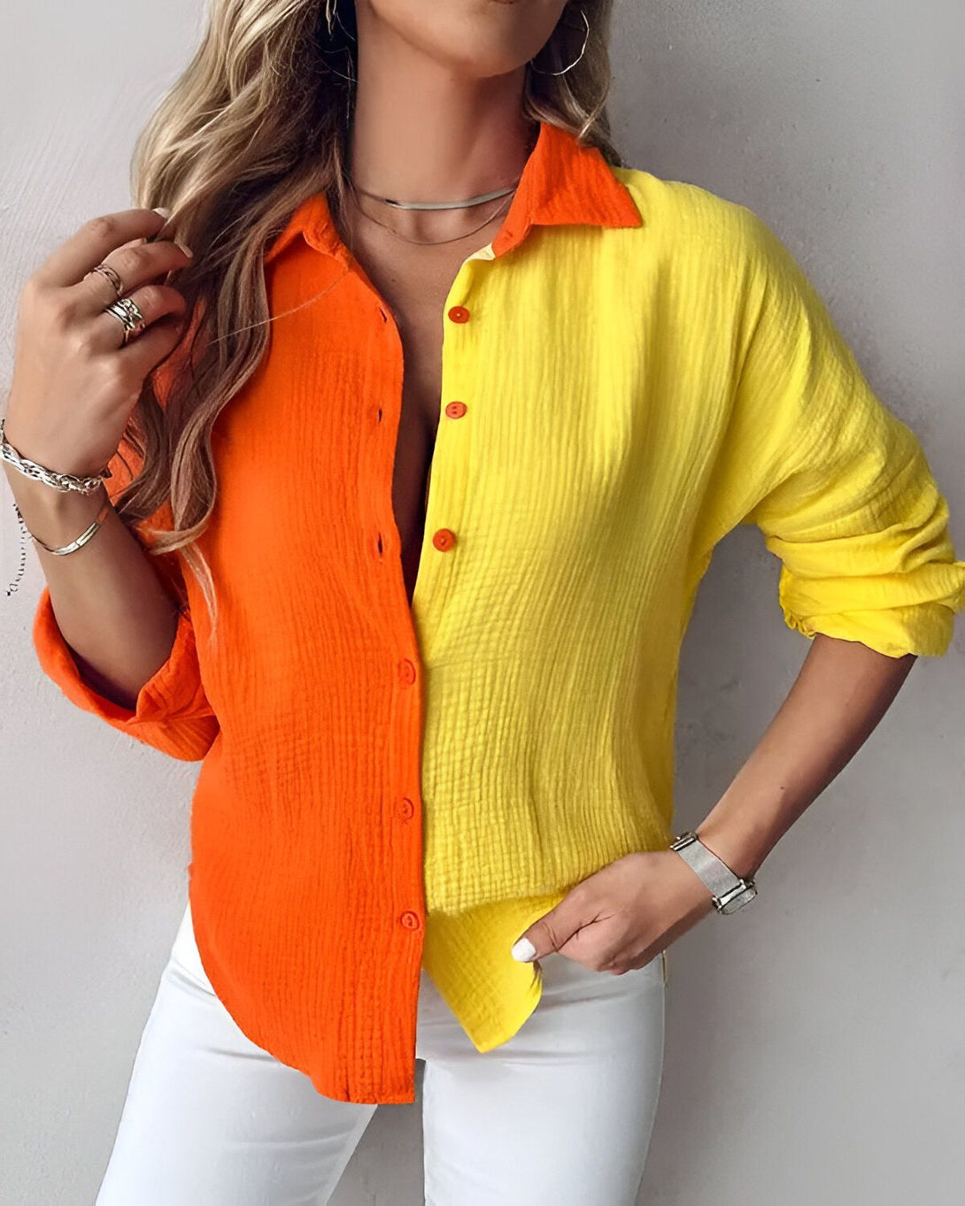 Une jeune femme porte une chemise orange et jaune. La chemise est ouverte et on peut voir son cou et ses clavicules. Elle porte également un collier et une montre.