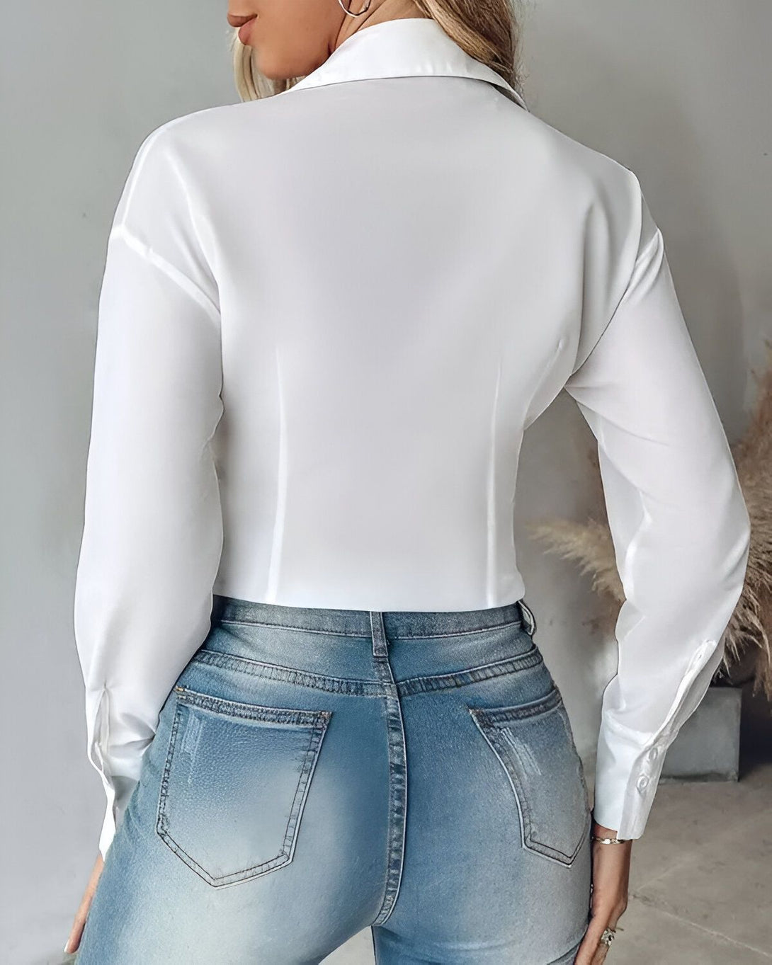 Une femme porte une chemise blanche et un jean bleu. La chemise est ouverte dans le dos et nouée au niveau de la taille.