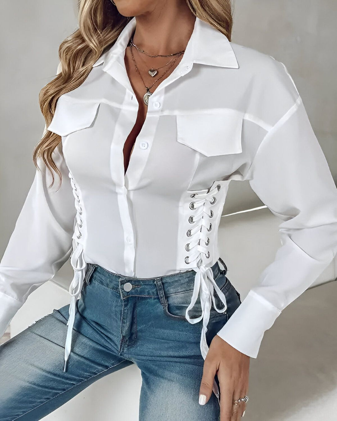 Une jeune femme porte une chemise blanche cintrée avec des lacets sur les côtés. Elle est associée à un jean bleu.