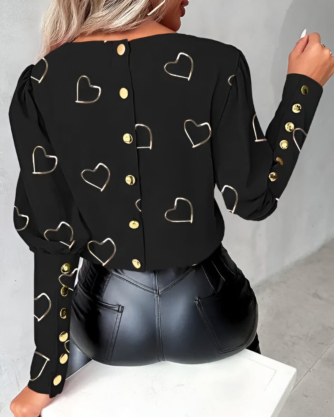 Une femme porte un chemisier noir avec des boutons en forme de cœur et des manches bouffantes.