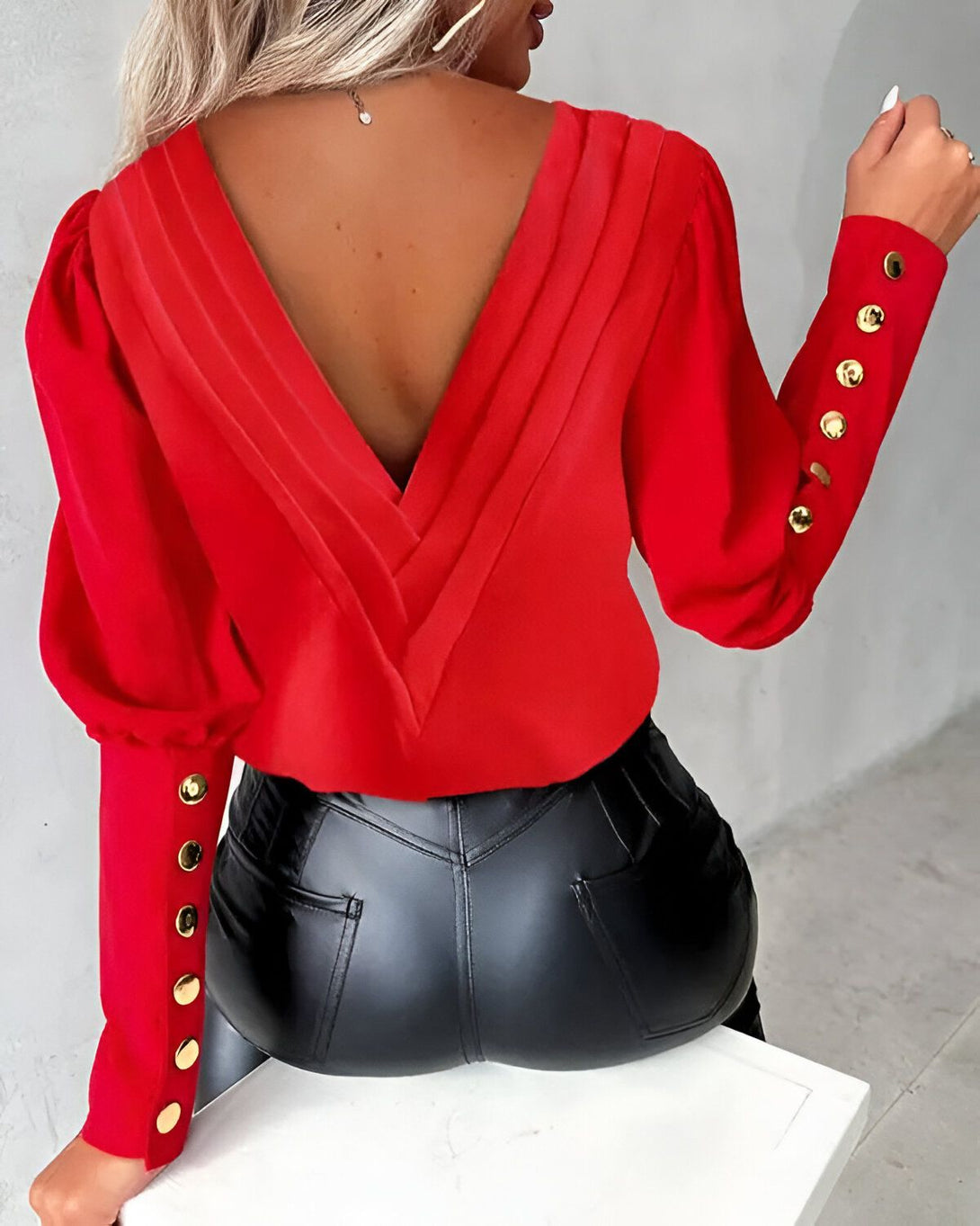 Une femme porte un chemisier rouge dos nu avec des boutons dorés.