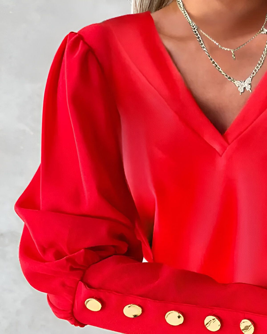 Une image d'une femme portant un chemisier rouge. Le chemisier est en soie et a des manches bouffantes. Il est également doté d'un col en V et de boutons dorés.