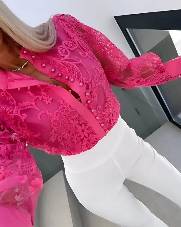 Une femme porte un chemisier rose en dentelle transparente avec des boutons et un pantalon blanc.