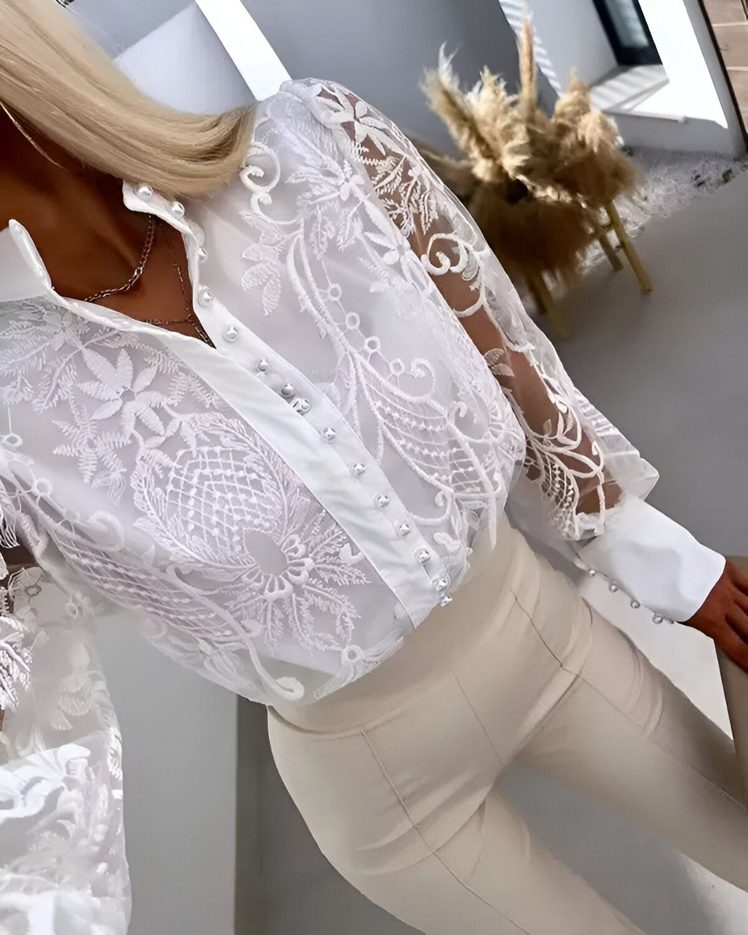 Une image d'une femme portant un chemisier blanc en dentelle avec des manches bouffantes et un pantalon beige.