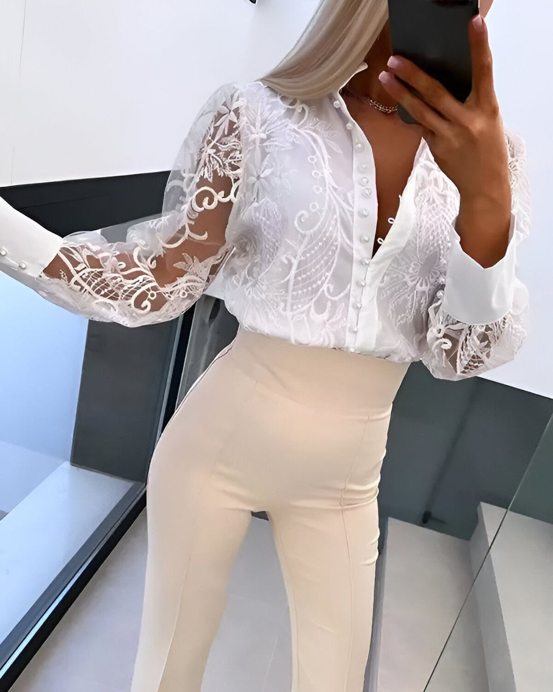 Une femme porte un chemisier blanc en dentelle avec des manches bouffantes et un pantalon beige taille haute.