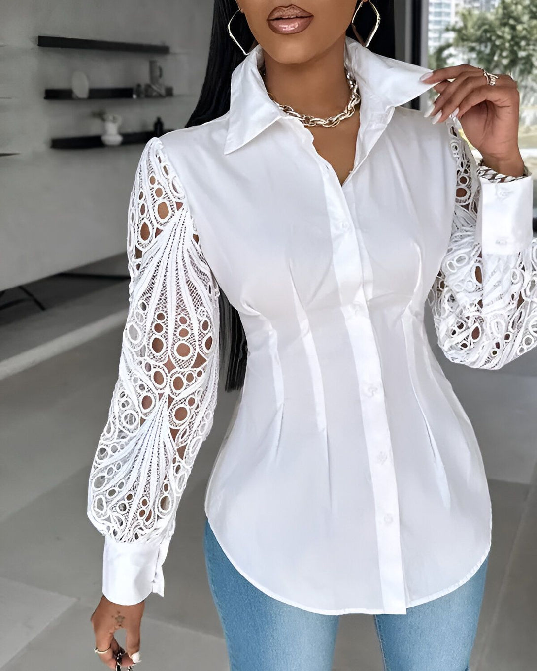 Une femme porte une chemise blanche cintrée avec des manches longues en dentelle. Elle est associée à un jean bleu.