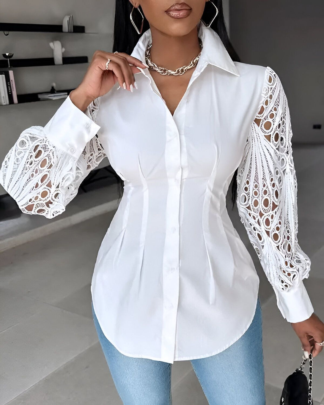 Une femme porte une chemise blanche cintrée avec des manches bouffantes en dentelle. Elle est associée à un jean bleu clair et des escarpins noirs.