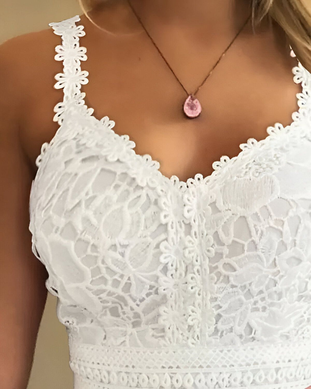 Une femme porte un haut blanc en dentelle avec un pendentif en forme de larme rose.