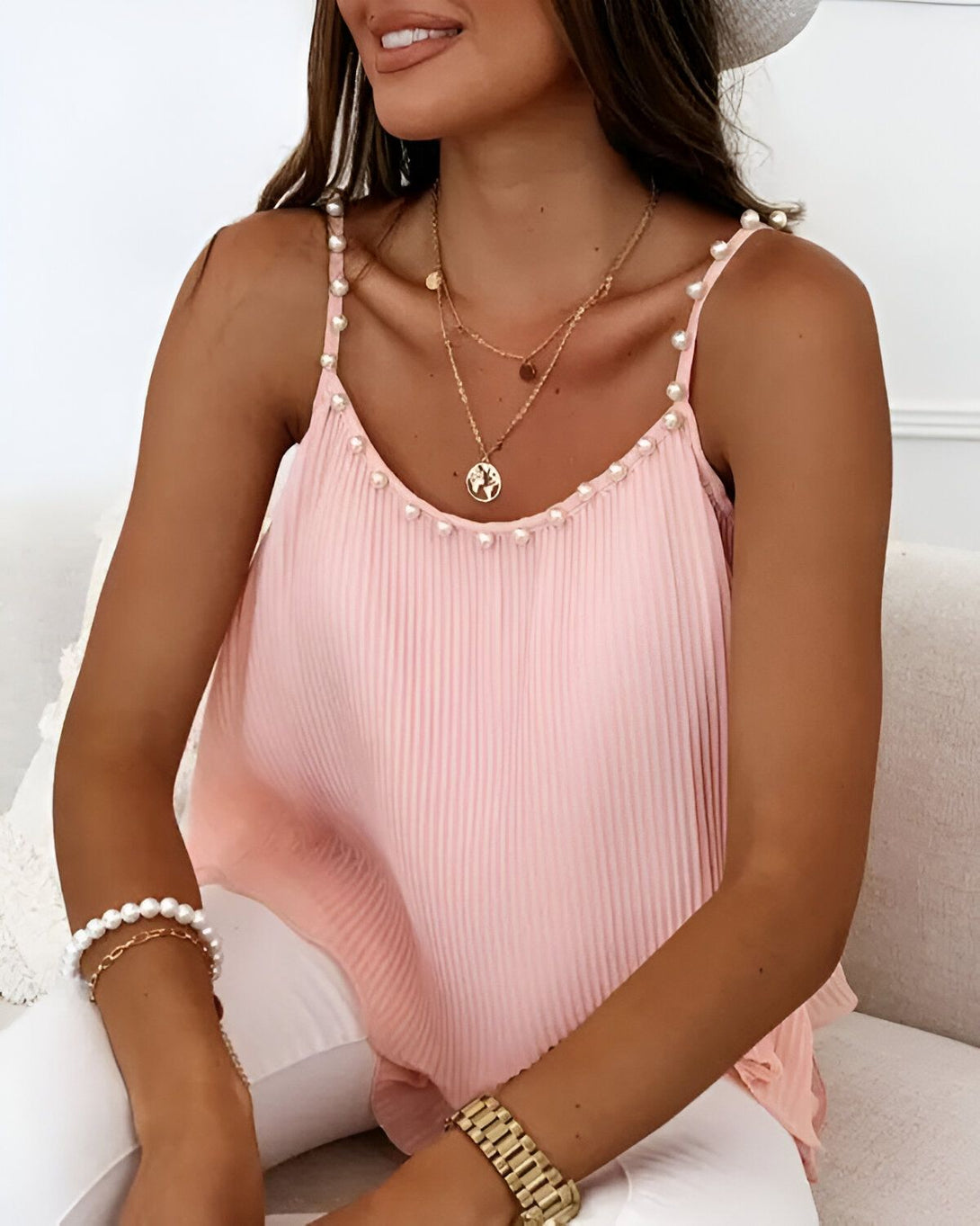 Une jeune femme porte un débardeur rose à bretelles avec des perles sur le devant. Elle porte également un collier avec un pendentif en forme de globe terrestre, un bracelet de perles et une montre.