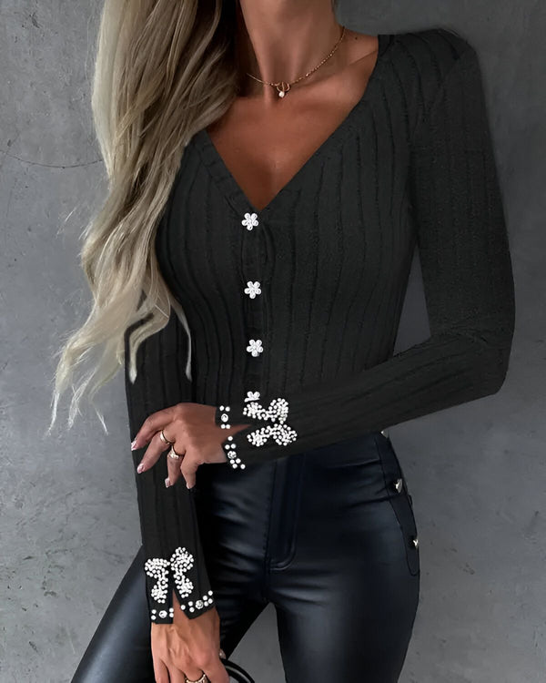 Une femme porte un chemisier noir avec des boutons blancs et des manches bouffantes. Elle porte également un pantalon en cuir noir et un collier de perles.