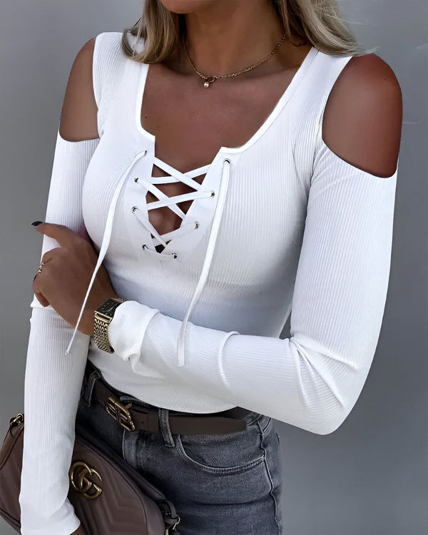 Une jeune femme porte un haut blanc à manches longues et à épaules dénudées. Le haut est noué sur le devant avec un laçage. Elle porte également un jean bleu et un collier.