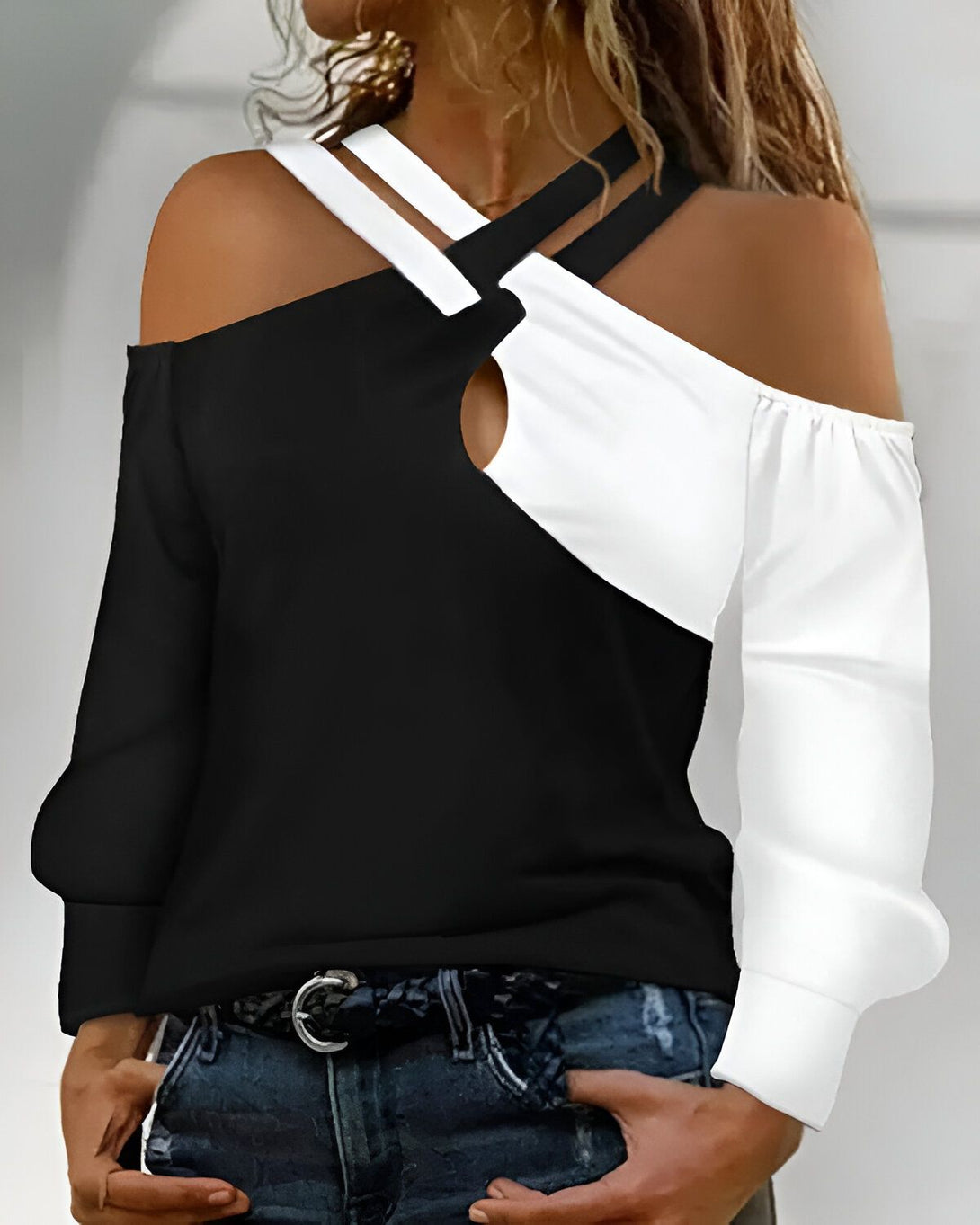 Une femme porte un haut noir et blanc à épaules dénudées. Le haut est croisé sur le devant et a un trou au niveau du décolleté. La femme porte également un jean bleu et une ceinture marron.