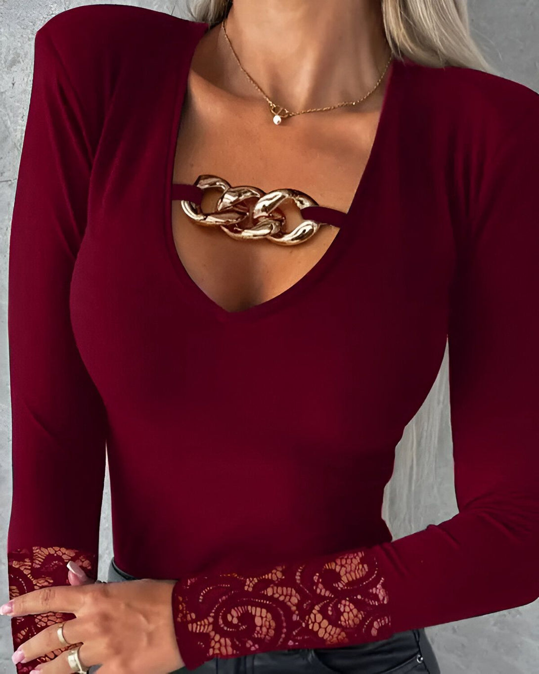Une femme porte un haut rouge à manches longues avec un bijou doré en forme de chaîne au niveau du décolleté. Le haut est moulant et met en valeur les courbes de la femme.