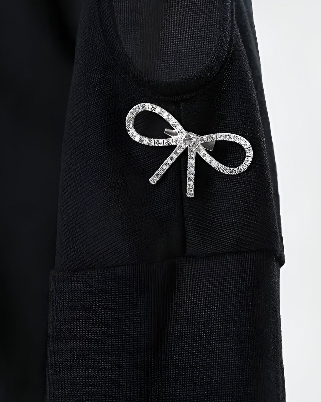 Une broche en forme de nœud en strass est épinglée sur une robe noire en tulle.