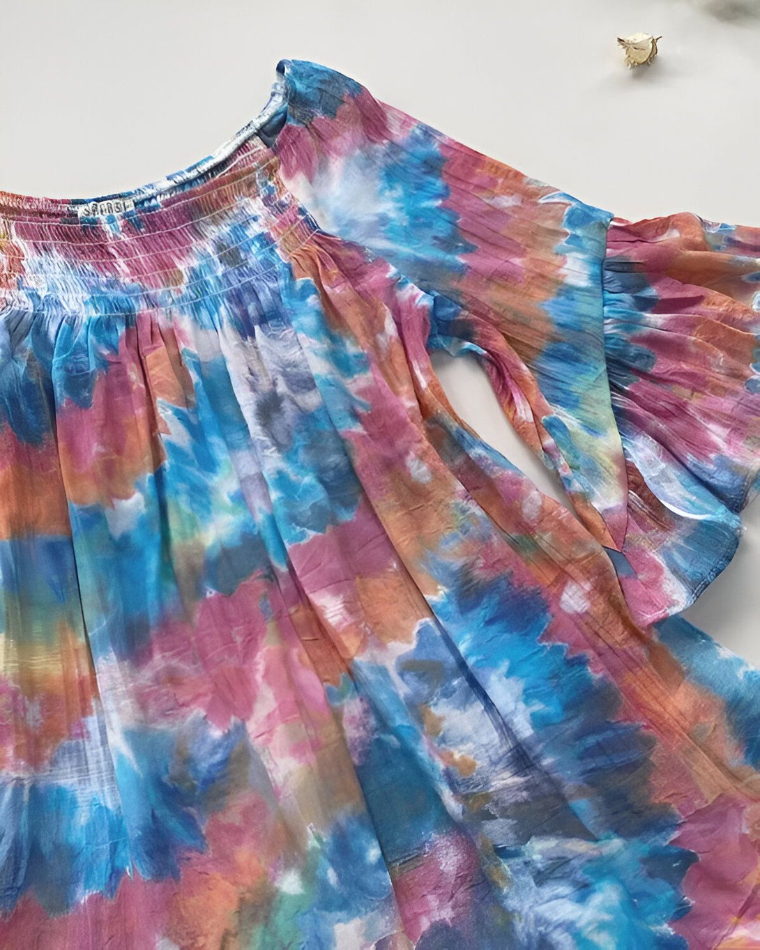 Une image d'une blouse tie-dye aux couleurs vives. La blouse a un col Bardot et des manches bouffantes.