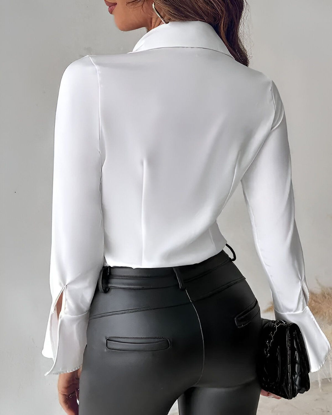 Une femme porte une chemise blanche cintrée et un pantalon en cuir noir.