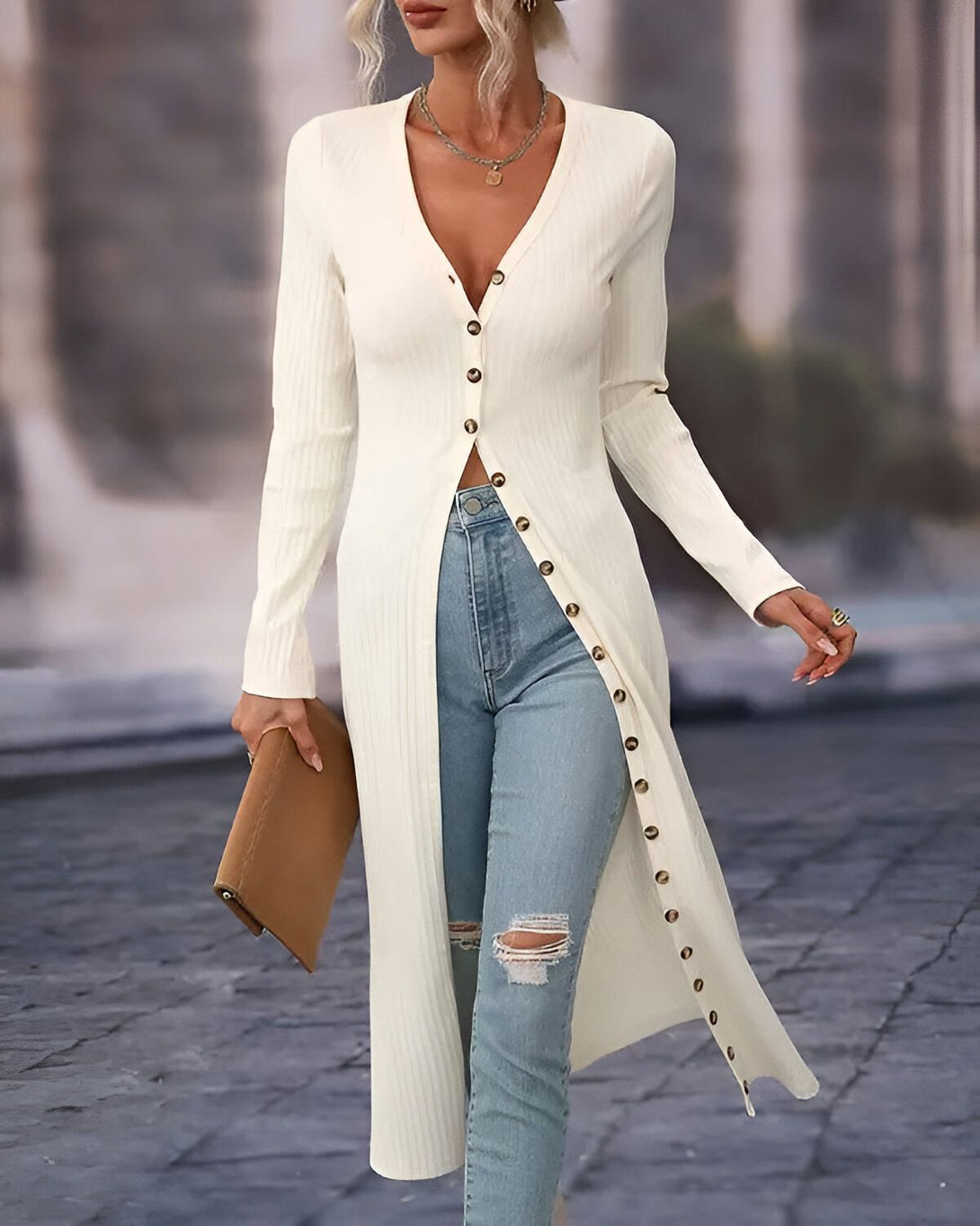 Une femme porte un long cardigan blanc avec des boutons sur le devant. Elle porte également un jean bleu déchiré et des talons hauts.