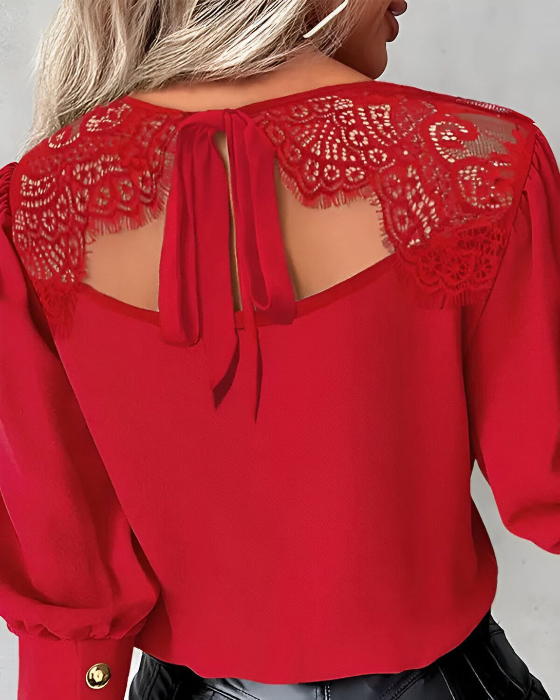 Une femme porte un chemisier rouge avec un dos en dentelle. Le chemisier est cintré et a des manches longues. La femme a les cheveux blonds et porte un collier.