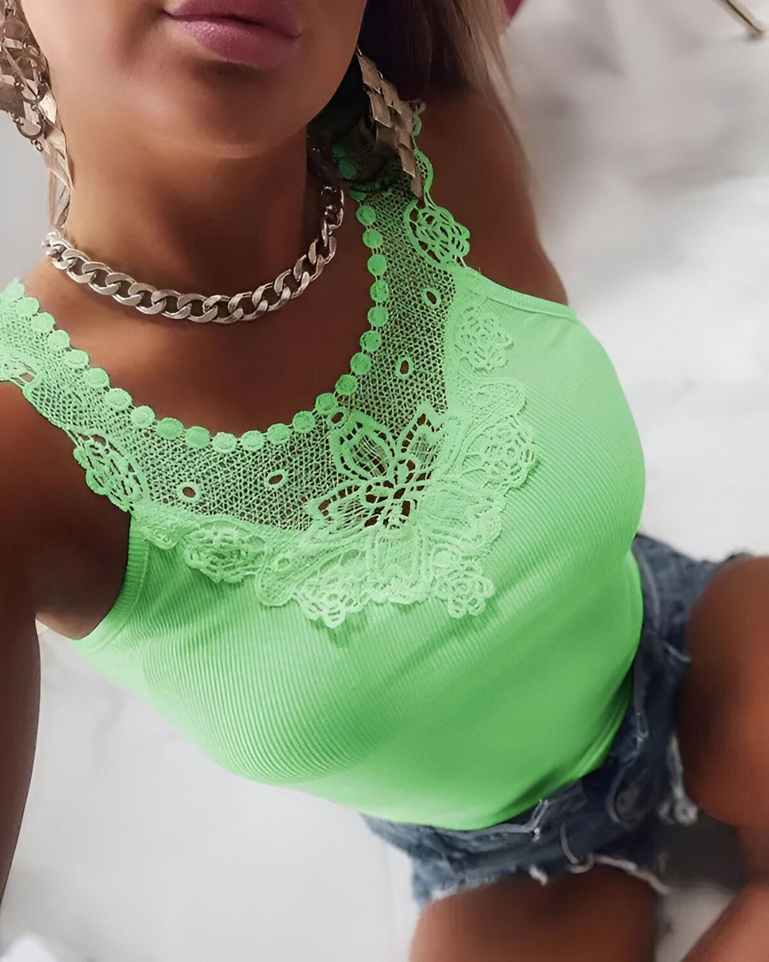 Une jeune femme porte un débardeur vert lime avec un col en dentelle blanche. Elle porte également un collier en chaîne argentée et un short en jean bleu.