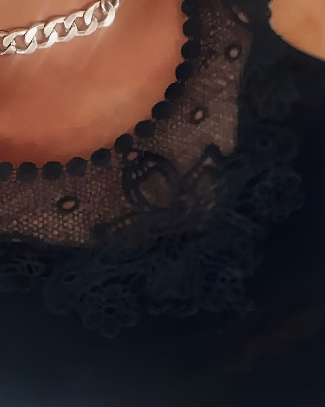 Une image d'une femme portant un collier en argent et un chemisier noir en dentelle.