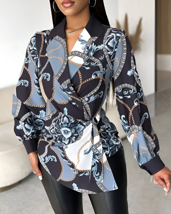 Une femme porte un chemisier noir à motifs bleus et blancs. Le chemisier est cintré à la taille et possède un col montant. La femme porte également un pantalon noir et des talons noirs.