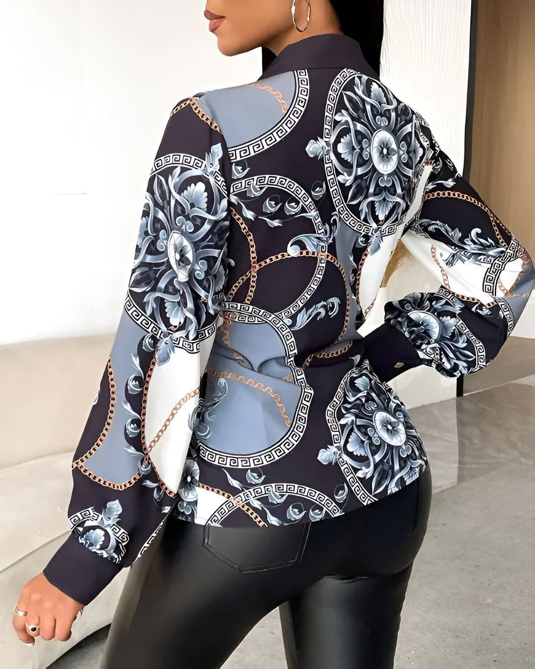 Une femme porte un chemisier noir et blanc à motifs baroques et chaînes. Le chemisier est cintré à la taille et possède des manches longues bouffantes.