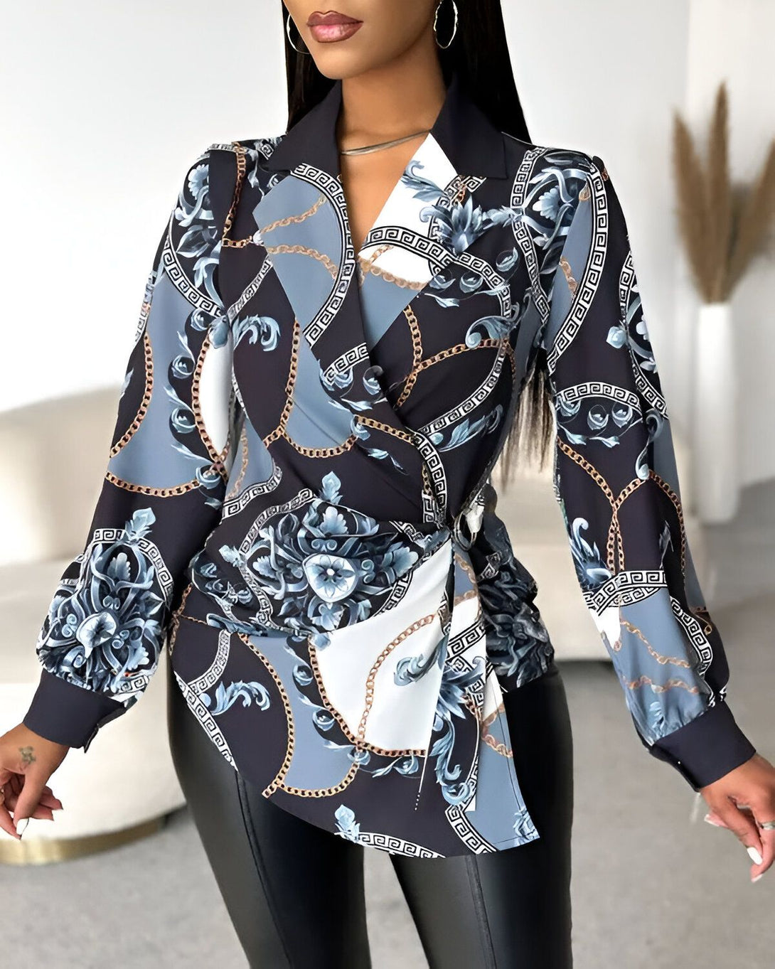 Une femme porte un chemisier noir et bleu à motifs baroques et chaînes. Le chemisier est cintré à la taille et possède un col montant. La femme porte également un pantalon en cuir noir et des escarpins noirs.