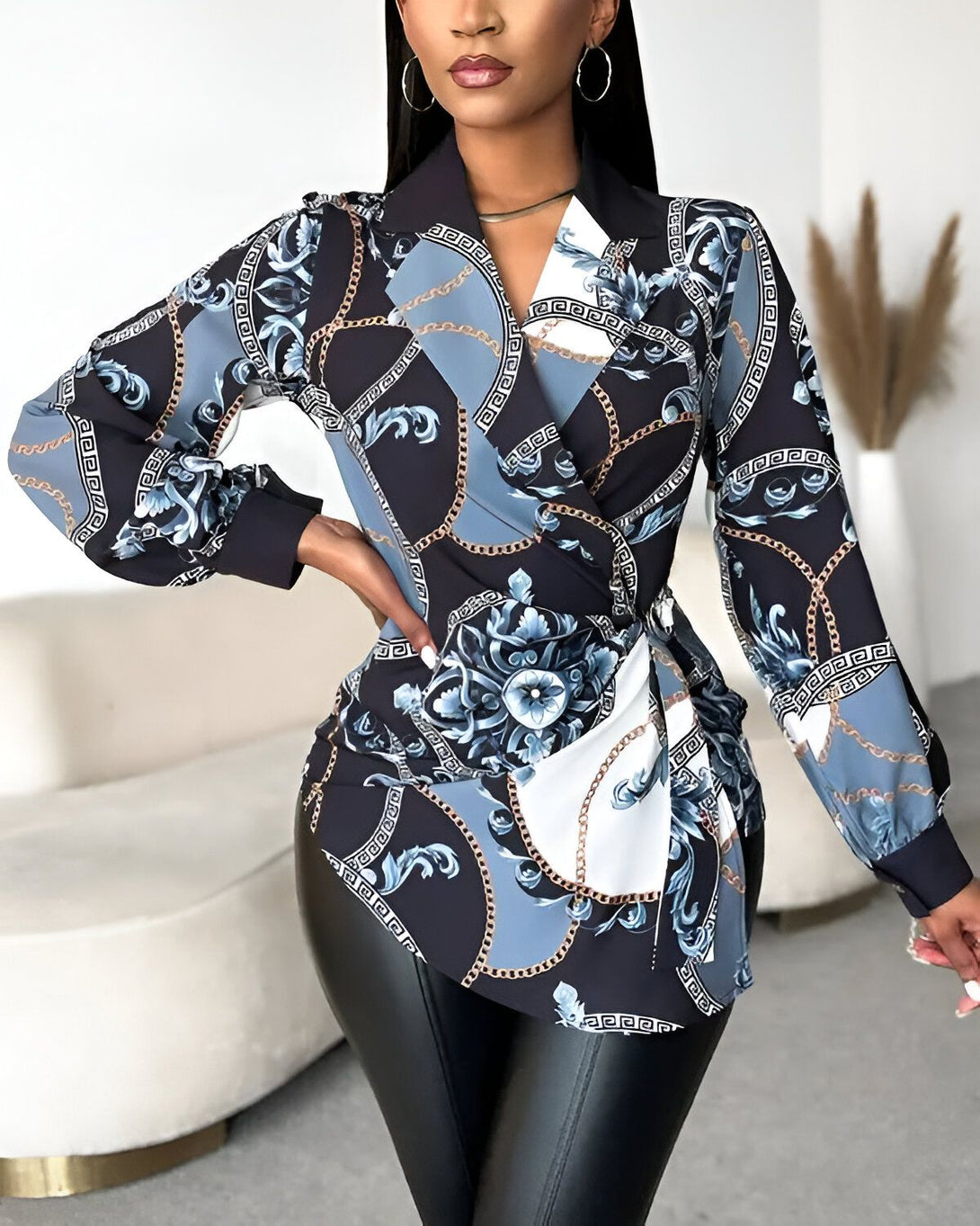 Une femme porte un chemisier bleu et noir à motifs. Le chemisier est cintré à la taille et possède un col montant. La femme porte également un pantalon noir en cuir.
