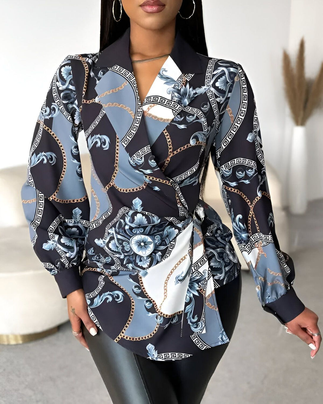 Une femme porte un chemisier noir et bleu à motifs baroques et chaînes. Le chemisier est cintré à la taille et possède un col montant. La femme porte également un pantalon en cuir noir.