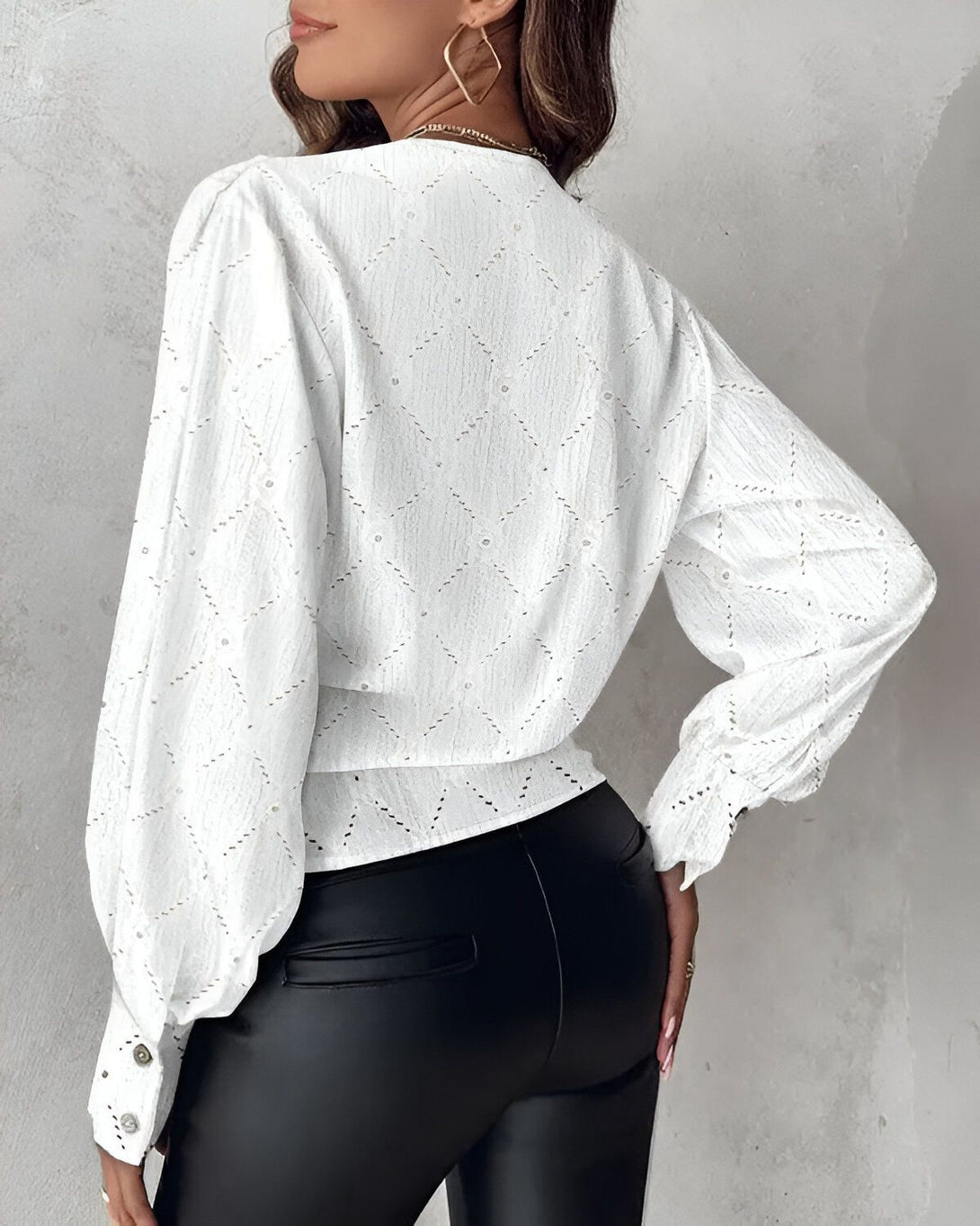 Une femme porte un chemisier blanc avec des motifs géométriques et des manches bouffantes. Le chemisier est rentré dans un pantalon noir.