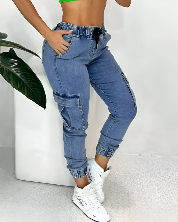 Une jeune femme porte un jean bleu clair taille haute avec des poches cargo sur les côtés. Elle porte également un haut vert et des baskets blanches.