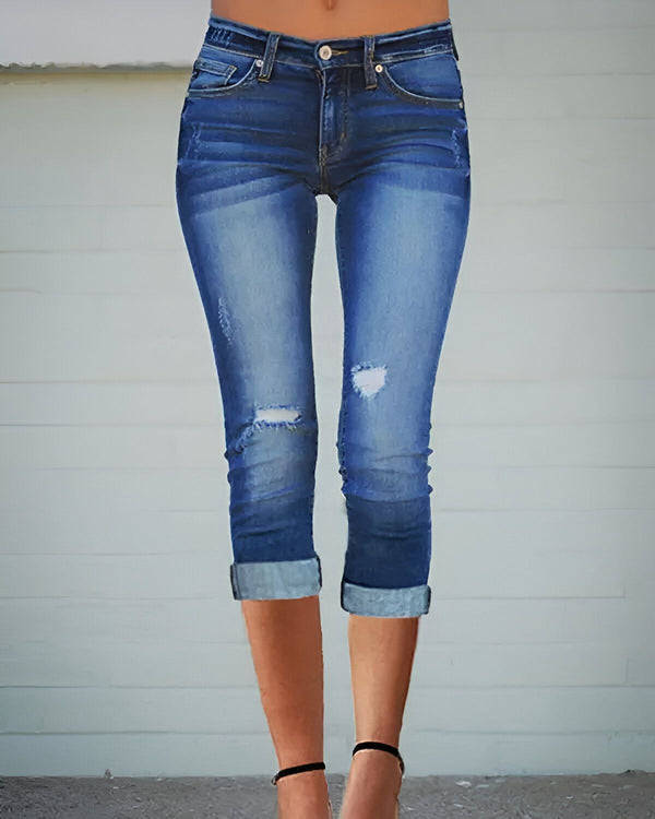 Une jeune femme porte un jean bleu troué et des talons noirs.