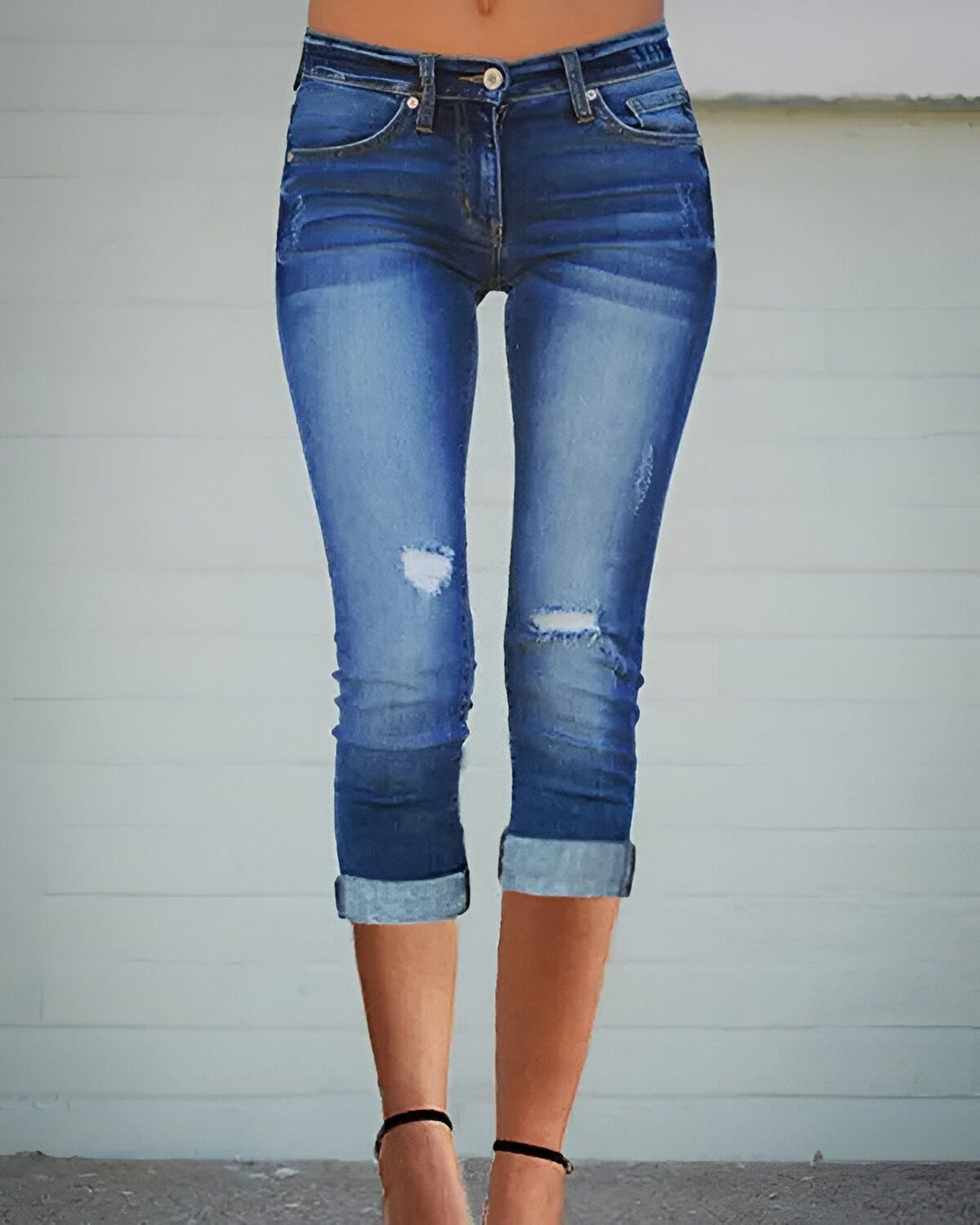 Une image d'une femme portant un jean bleu troué et retroussé au niveau des mollets. Elle porte des talons noirs.