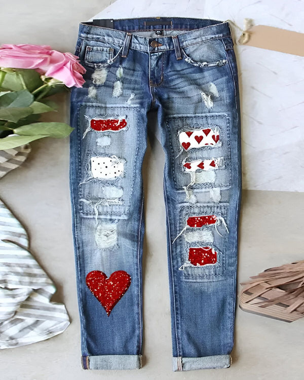 Une image d'un jean bleu déchiré avec des patchs en forme de cœur rouge et blanc.