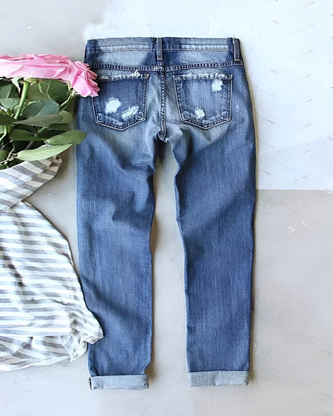 Une image d'un jean bleu troué avec des roses roses et un t-shirt gris à rayures blanches posé à côté.