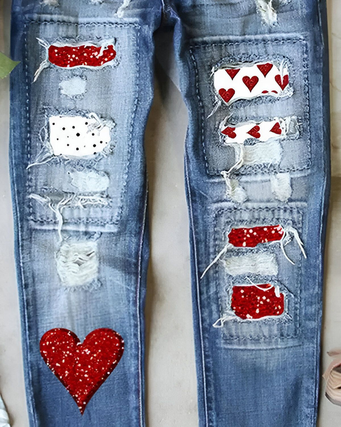 Le jean est bleu troué avec des patchs en forme de coeurs rouges à paillettes et de pois blancs.