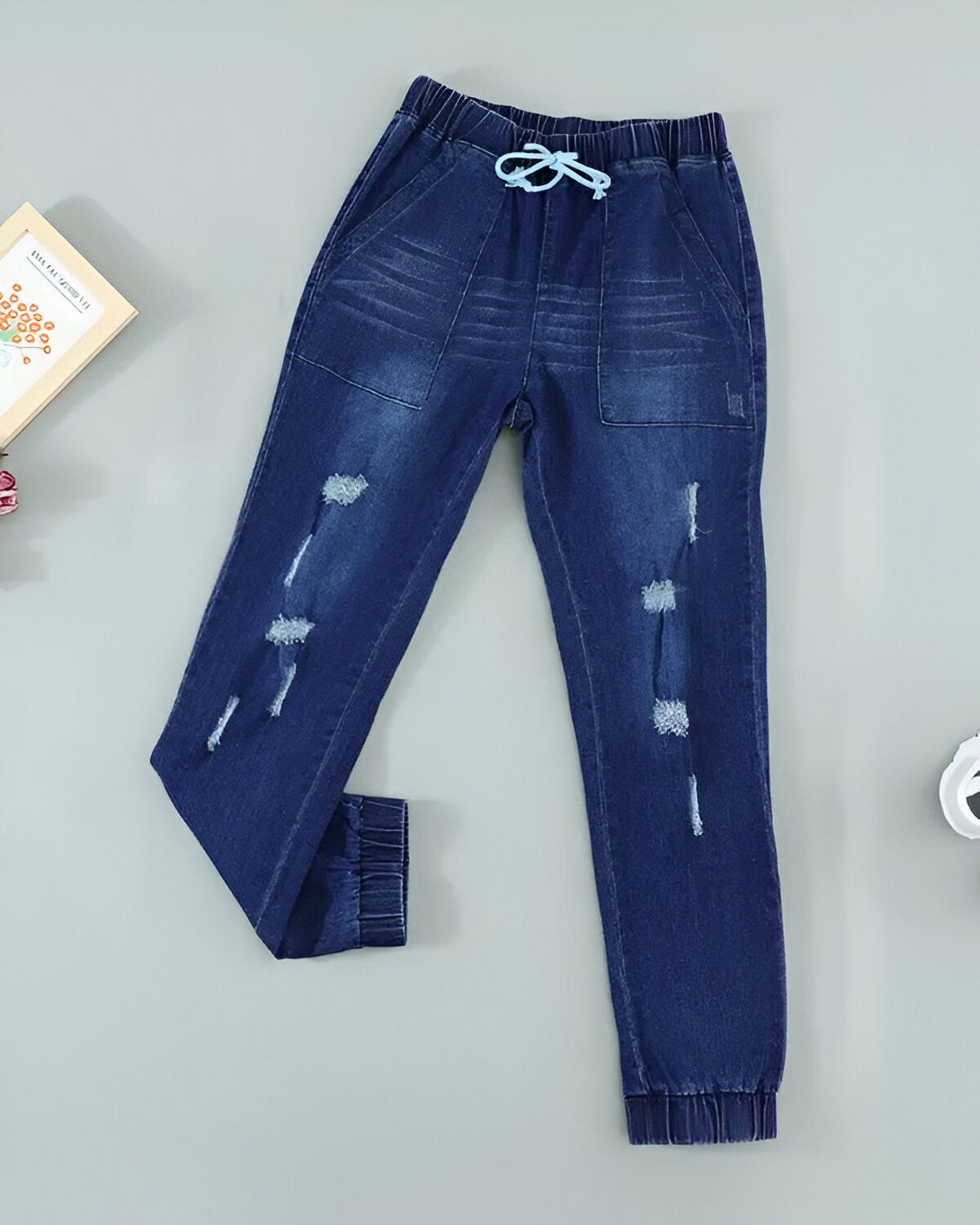 Un jean bleu troué avec un cordon de serrage à la taille.